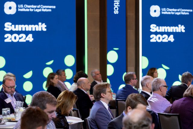 A full room of attendees at ILR Summit 2024, seated at round tables beneath the Summit 2024 screens